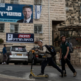 Unos niños pasan junto a un edificio residencial adornado con pancartas electorales de los partidos Sionismo Religioso (arriba) y Judaísmo Unido de la Torá (abajo) en Jerusalén, en la víspera de las elecciones al Knéset