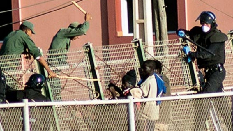 Agentes de la Guardia Civil y las fuerzas auxiliares marroquíes tratan de impedir que que varias personas migrantes salten la valla de Melilla.- CAMINANDO FRONTERAS