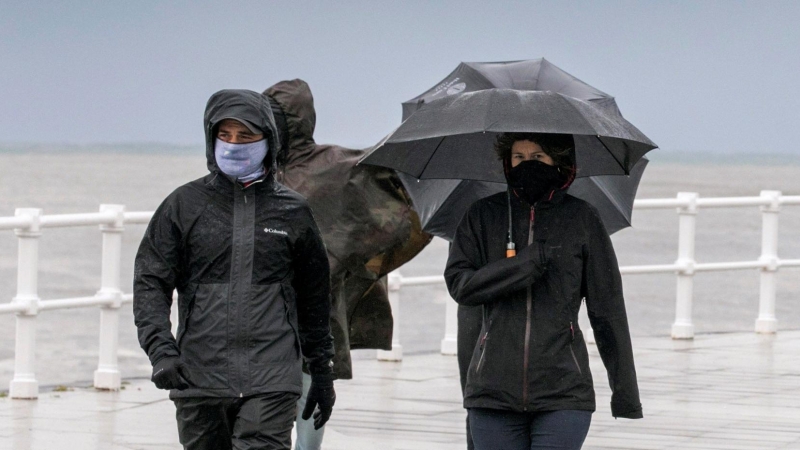 Un grupo de personas paseando por la playa de San Lorenzo de Gijon, bajo un fuerte chubasco y viento - EFE/Alberto Morante