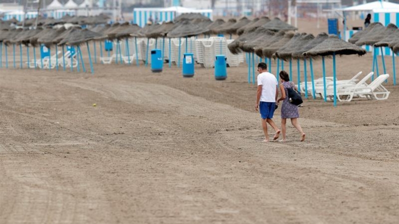 Una pareja pasea por la playa de la Malvarrosa en la que la afluencia de gente ha descendido notablemente debido en gran medida al descenso de temperaturas, a los chubascos y al cielo nublado. /EFE