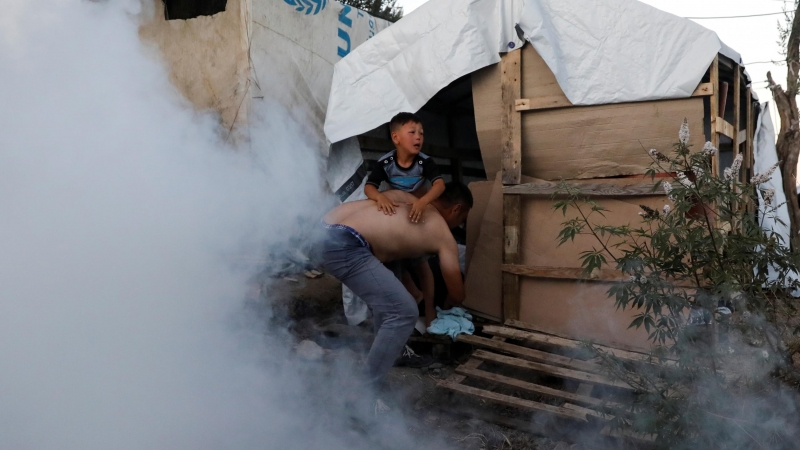 Un solicitante de asilo carga con su hijo para alejarlo de los gases lacrimógenos lanzados por la policía para sofocar las protestas de los refugiados el pasado domingo en el campo de refugiados de Moria, en la isla de Lesbos, Grecia.-REUTERS
