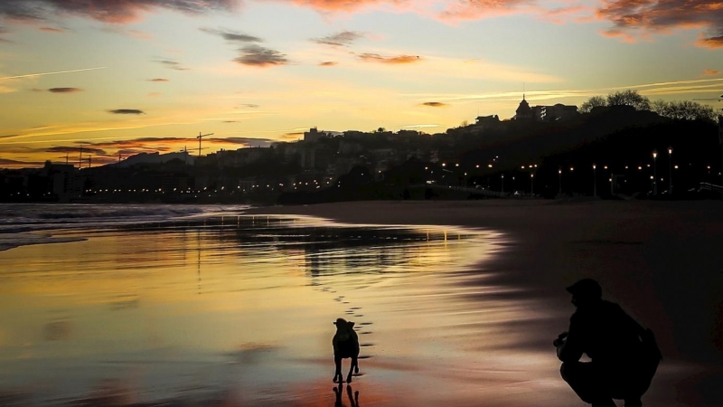 SAN SEBASTIÁN (GIPUZKOA), 14/01/2020.- Un hombre juega con su perro al amanecer en la playa de Ondarreta de San Sebastián, donde este martes los cielos en el País Vasco se presentan con intervalos nubosos, las temperaturas mínimas subirán y las máximas s