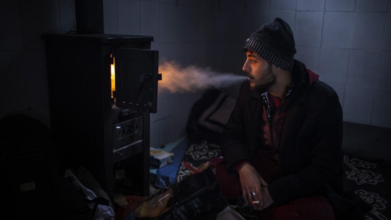 Yousef, de 27 años, fuma un cigarrillo frente a la estufa en el interior de una cabaña que utiliza para dormir durante su travesía por las montañas de Bosnia para cruzar la frontera. JM López.