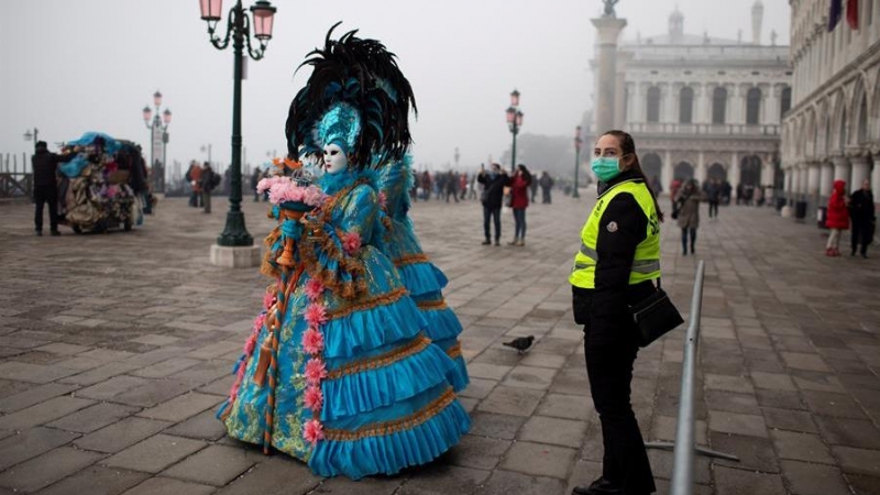 Un guardia de seguridad con una máscara protectora junto a personas disfrazadas paseando por las calles de Venecia cerca de la plaza San Marco. EFE