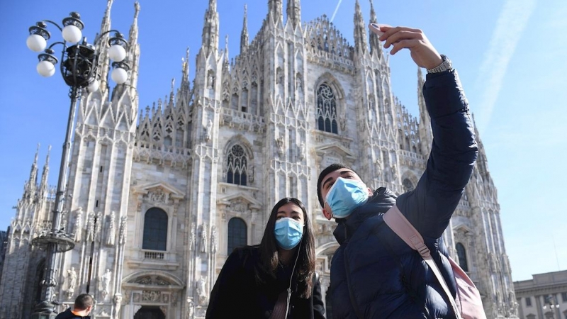 Dos turistas con mascarilla se hacen una fotografía junto a la catedral de Milán. - EFE