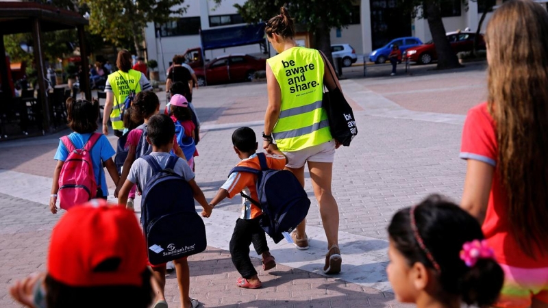 Voluntarios ayudan a cruzar a varios niños en una isla griega. / REUTERS