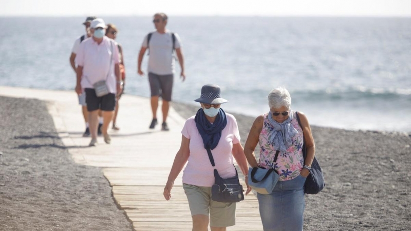 Varios turistas pasean este viernes por las inmediaciones del hotel en el que desde el pasado lunes permanecen incomunicados sus huéspedes y trabajadores al dar positivo en coronavirus cuatro de los que se alojaban en el centro turístico de Adeje, en el s