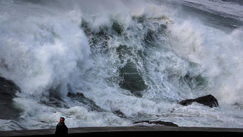 Un hombre pasea este domingo ajeno a una gran ola a punto de romper en el Paseo Nuevo de San Sebastián. EFE