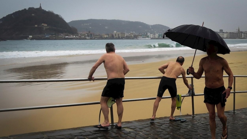 Varios hombres se bañan este martes en la playa de Ondarreta de San Sebastián a pesar del frío y la lluvia. EFE