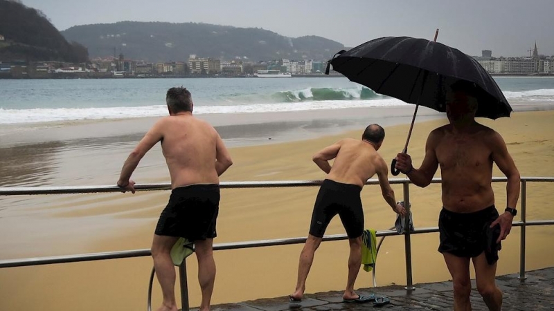 Varios hombres se bañan este martes en la playa de Ondarreta de San Sebastián a pesar del frío y la lluvia. EFE