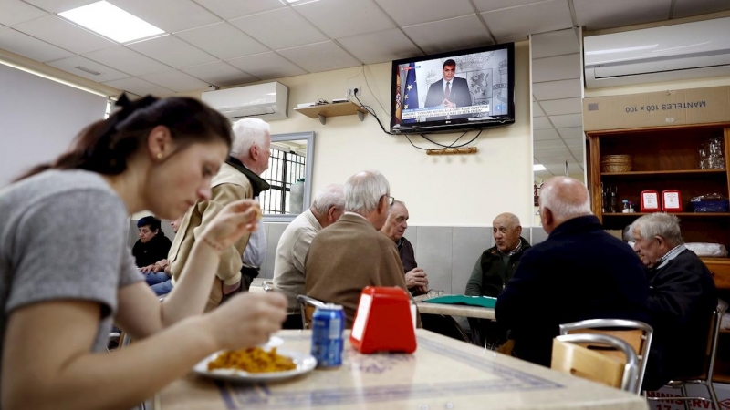 12/03/2020.- Un grupo de ancianos juega a las cartas este jueves en un bar del barrio de Aluche, en Madrid, mientras en la televisión comparece el presidente del Gobierno por el coronavirus. / EFE - MARISCAL