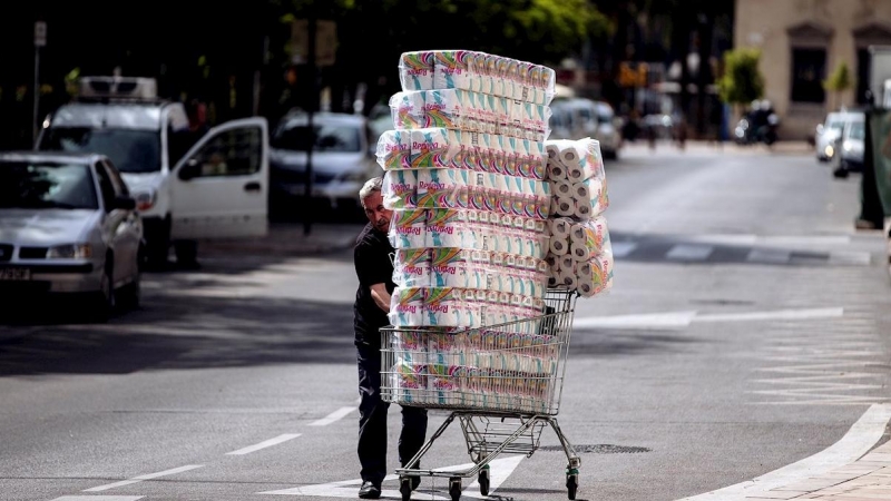 Un trabajador transporta numerosos rollos de papel higiénico en un carro de la compra dirección a un comercio en el centro de Málaga. - EFE