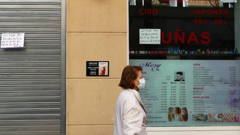 Una mujer usa una mascarilla mientras pasa por una peluquería cerrada propiedad de residentes chinos en Madrid. REUTERS / Sergio Perez