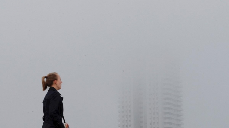 Una persona pasa junto a un edificio envuelto en niebla en Valencia. EFE