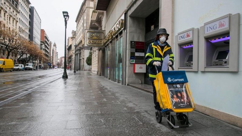Una trabajadora del servicio de Correos realiza su trabajo por las calles casi desiertas de Zaragoza el pasado lunes. EFE/Javier Cebollada