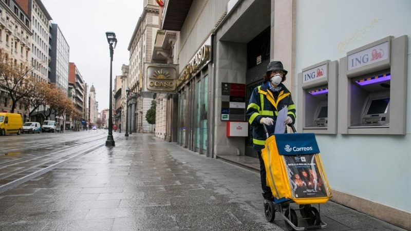 Una trabajadora del servicio de Correos realiza su trabajo por las calles casi desiertas de Zaragoza el pasado lunes. EFE/Javier Cebollada