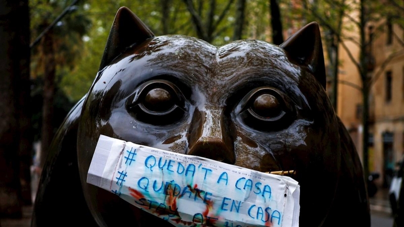 Una mascarilla de fabricación casera con la advertencia ‘’Quedate en casa’’ protege la boca de la escultura 'El gato', del escultor colombiano Fernando Botero, en la Rambla del Raval de Barcelona, este lunes en el que los españoles encaran una nueva seman