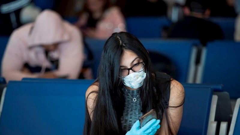 Una mujer, con mascarilla, consulta su teléfono móvil.- EFE