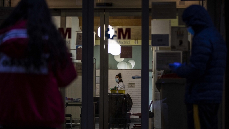 Las puertas de un hospital madrileño muestran personas esperando con mascarillas y guantes y una trabajadora sanitaria. / JAIRO VARGAS