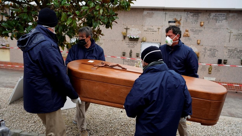 Los empleados de una morgue llevan el ataúd de una persona que murió por la enfermedad del coronavirus (COVID-19), durante el cierre parcial para combatir el brote de la enfermedad, en el cementerio de Carabanchel en Madrid, España, el 27 de marzo de 2020