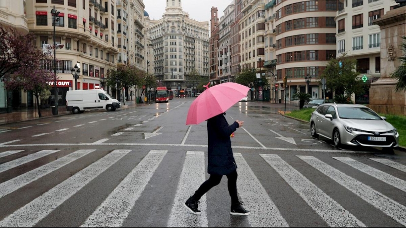 Un hombre protegido con paraguas en la plaza del Ayuntamiento de Valencia prácticamente vacía durante el decimoséptimo día del estado de alarma decretado por el Gobierno. EFE/Kai Försterling