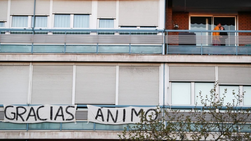 Una pareja se besa en el balcón junto a una pancarta de un vecino que reza 'gracias' y 'ánimo'. Sergio Pérez/Reuters