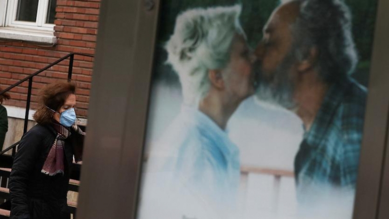 Una mujer llevando mascarilla frente a un cartel publicitario de una pareja besándose. REUTERS