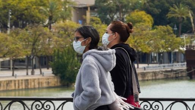 Dos jovenes con mascarillas paseando andando por el puente de Triana. /EUROPA PRESS/Archivo