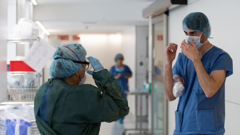 Un professional sanitari ajuda una companya a protegir-se abans d'atendre un pacient amb covid-19, en un dels blocs quirúrgics de l'Hospital Clínic de Barcelona habilitat com a UCI en la pandèmia de coronavirus. ACN/ Francisco Àvia / Hospital Clínic