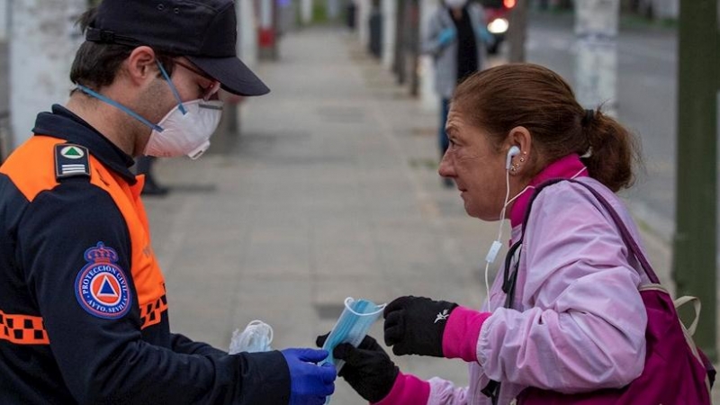 Voluntarios de Protección Civil repartiendo mascarillas a los viajeros que a primera hora de la mañana utilizaban los autobuses urbanos de Sevilla para su traslado a los puestos de trabajo. EFE/Julio Muñoz