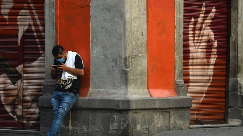 Un hombre observa su teléfono móvil en una calle del centro histórico de Ciudad de México. México extenderá las medidas de distanciamiento social hasta el 30 de mayo. - EFE
