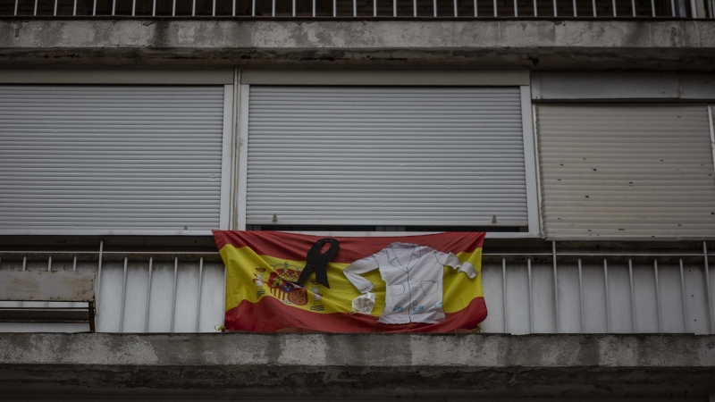 Una bandera de España con crespón negro, junto a un uniforme sanitario en un balcón de la calle Antonio López de Madrid.-JAIRO VARGAS