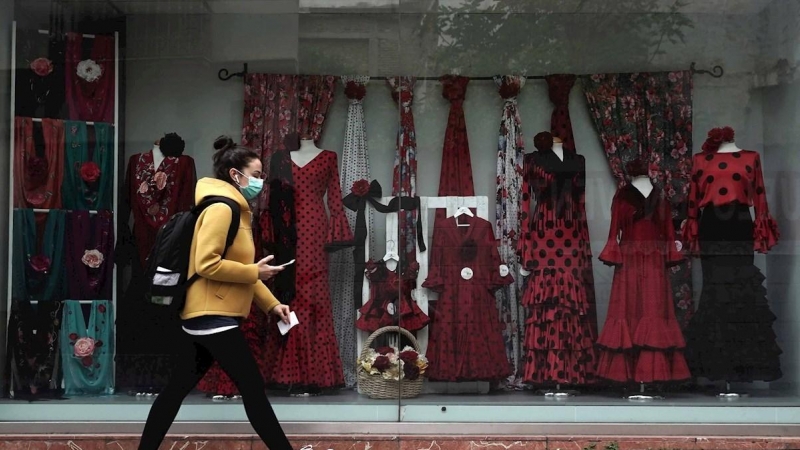 22/04/2020.- Una mujer con mascarilla camina junto a un escaparate de una tienda. / EFE - RAFA ALCAIDE