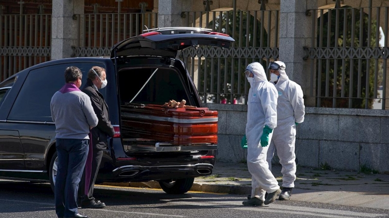 Operarios con trajes de protección se disponen a introducir un ataúd en un cementerio para su entierro, ante la mirada de los pocos familiares que han podido asistir por las limitaciones establecidas debido al estado de alarma decretado por el gobierno pa