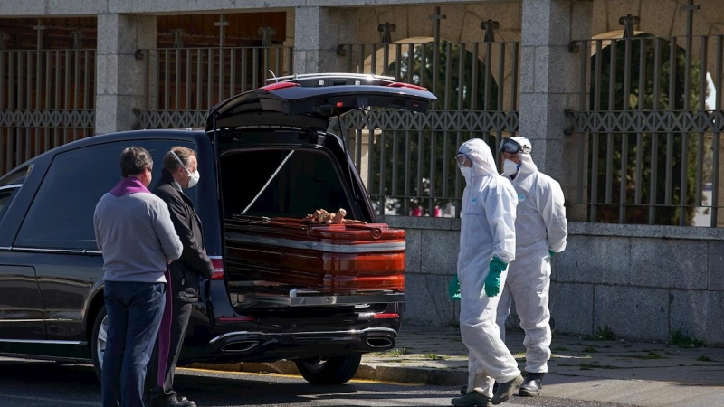 Operarios con trajes de protección se disponen a introducir un ataúd en un cementerio para su entierro, ante la mirada de los pocos familiares que han podido asistir por las limitaciones establecidas debido al estado de alarma decretado por el gobierno pa