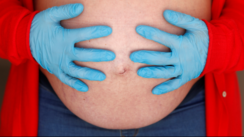 Una embarazada de 9 meses usa guantes mientras se toca el vientre durante el confinamiento por coronavirus. REUTERS / Jon Nazca
