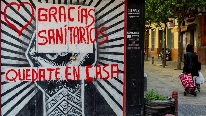 Una mujer con un carro de la compra pasa junto a un comercio cerrado con una pintada de agradecimiento a los sanitarios en una céntrica calle de Sevilla, hoy miércoles en la séptima semana de confinamiento decretado en el Estado de Alarma debido a la cris