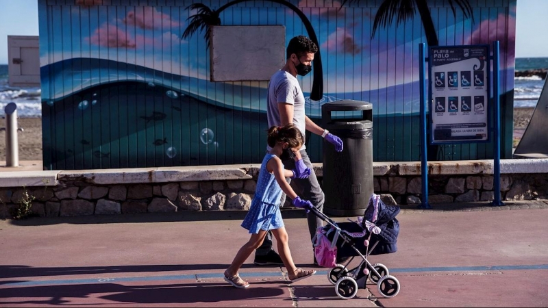Un hombre y su hija pasean ataviados con mascarillas por la playa del Palo en Málaga. - EFE