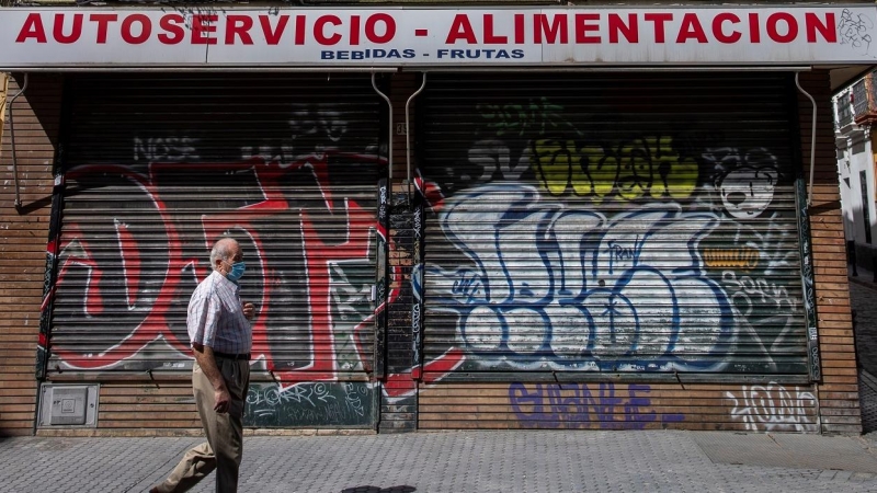 Un hombre protegido con mascarilla camina ante un comercio cerrado en una céntrica calle de Sevilla, durante el confinamiento decretado en el Estado de Alarma debido a la crisis sanitaria de la covid-19. EFE/Julio Muñoz