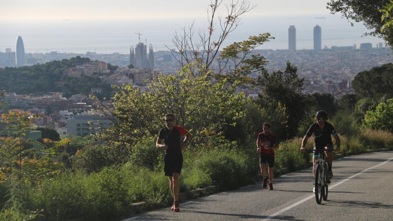 Pla general d'un ciclista i dos corredors pujant pel carrer Manuel Arnús, just abans d'arribar a la carretera de les Aigües, al Parc de Collserola de Barcelona. Imatge del 2 de maig de 2020. (Horitzontal)