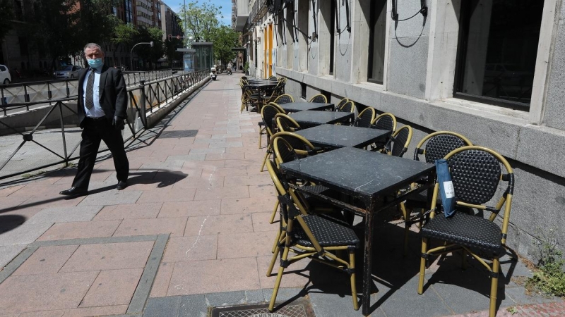 Un hombre con mascarilla pasa junto a una terraza cerrada de un bar en Madrid. E.P./Marta Fernández