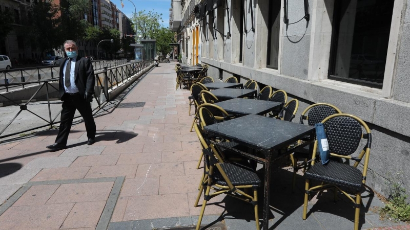 Un hombre con mascarilla pasa junto a una terraza cerrada de un bar en Madrid. E.P./Marta Fernández