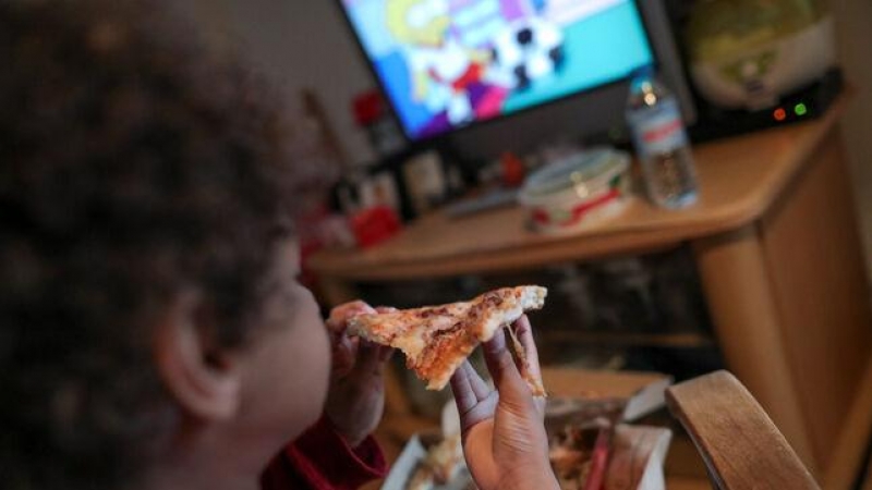 Un niño come un trozo de pizza del menú infantil de Telepizza mientras ve la televisión en su casa. EUROPA PRESS / JESÚS HELLÍN