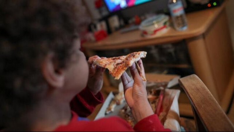 Un niño come un trozo de pizza del menú infantil de Telepizza mientras ve la televisión en su casa. EUROPA PRESS / JESÚS HELLÍN