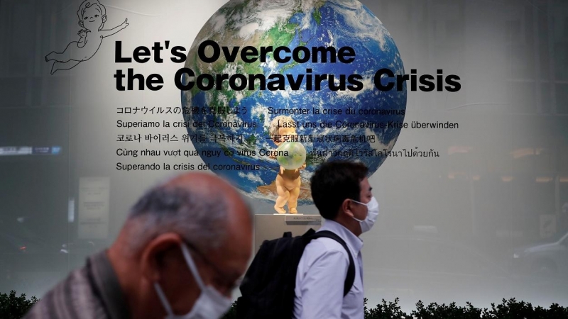 Dos peatones con mascarilla pasan por delantedel escaparate de unos grandes almacenes en Tokio, donde un cartel dice 'Vamos a superar la crisis del coronavirus'. REUTERS / Kim Kyung-Hoon