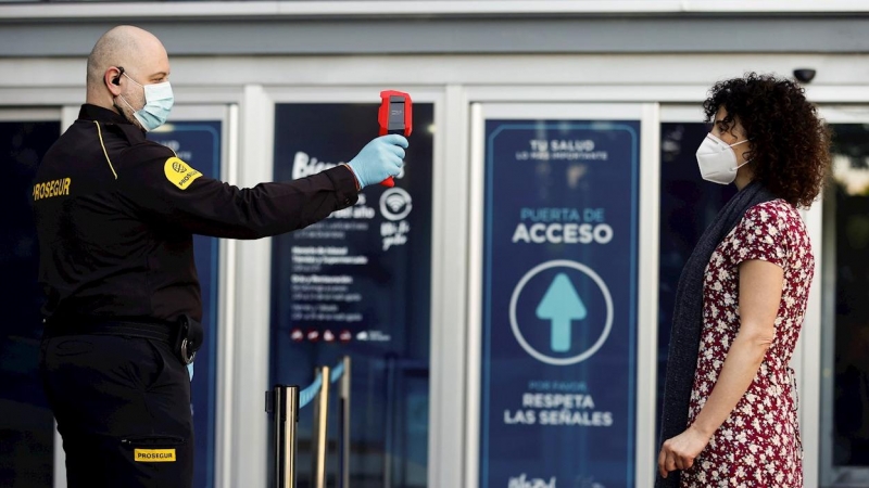 19/05/2020.-  Una persona de seguridad  toma la temperatura corporal a una mujer en un centro comercial. / EFE - CHEMA MOYA