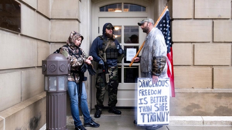 Manifestantes contra las medidas de confinamiento decretadas por el gobernador de Michigan, Gretchen Whitmer, se refugian de la lluvia en una de las entradas del Capitolio del Estado, en la localidad de Lansing. REUTERS/Seth Herald