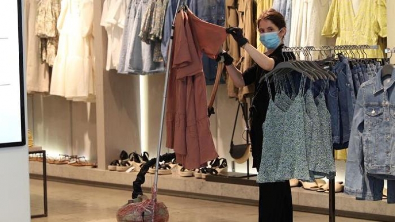 Una dependienta desinfecta la ropa con una plancha de vapor en el interior de una tienda. EFE/Rodrigo Jiménez