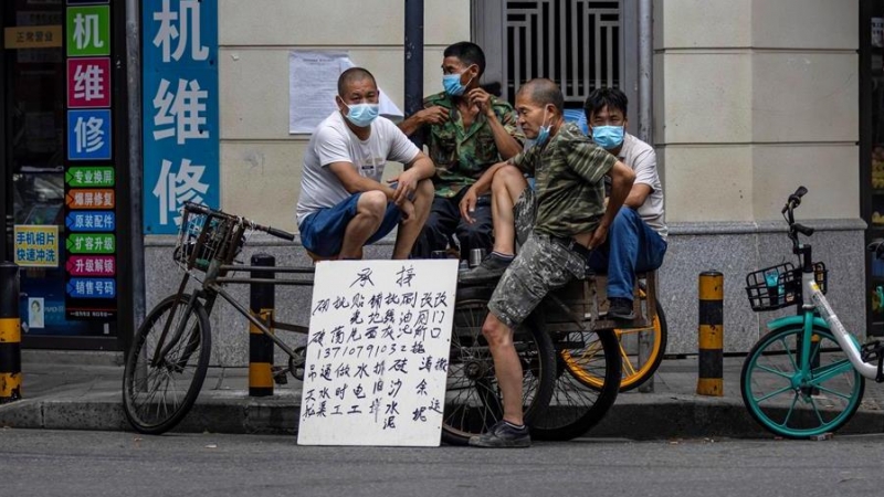 Varios obreros de la construcción aguardan en la calle junto a un cartel en el que ofrecen sus servicios en Cantón (China) / EFE