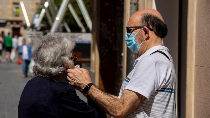 Un hombre ayuda a ponerse la mascarilla a una mujer en el centro de Vitoria este jueves, en el que ha entrado en vigor la obligatoriedad de llevar mascarillas en espacios públicos, ya sea al aire libre o cerrados, siempre y cuando no se pueda mantener una